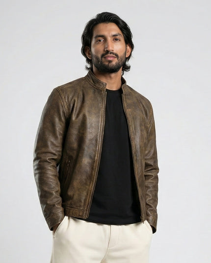 Man wearing a brown leather jacket over a black shirt with white pants on a light gray background