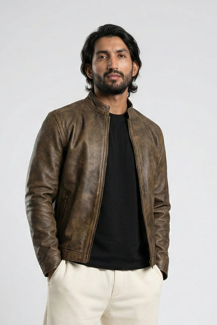 Man wearing a brown leather jacket over a black shirt with white pants on a light gray background