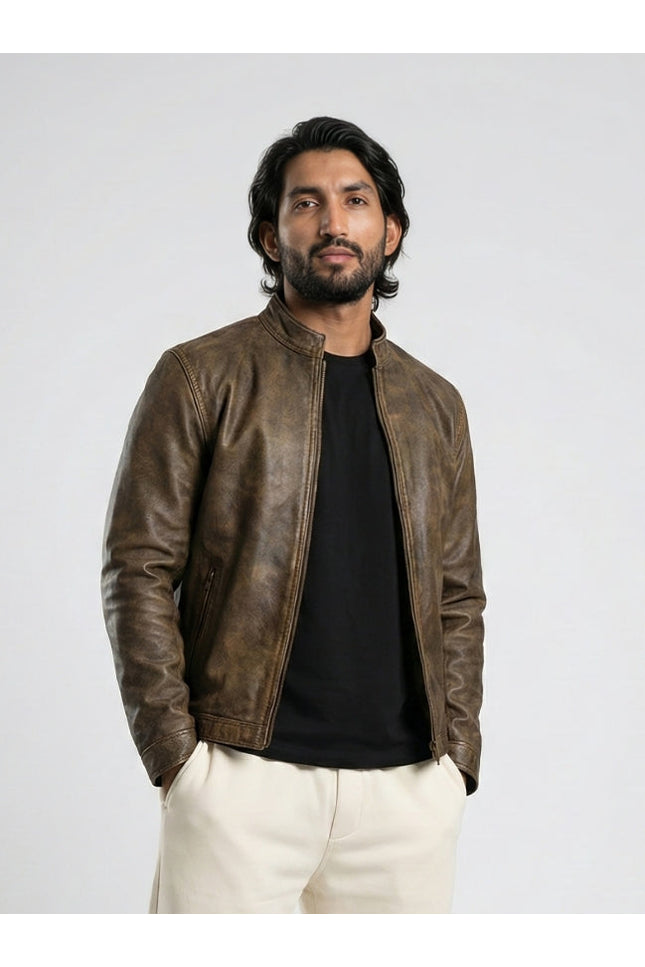 Man wearing a brown leather jacket over a black shirt with white pants on a light gray background