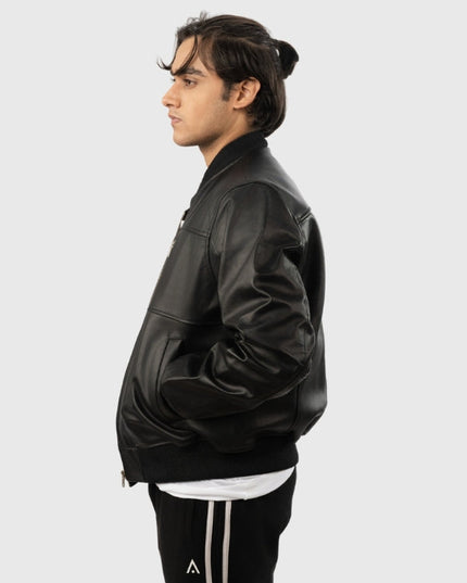 Person wearing a black leather jacket and black pants with white stripes on a light gray background
