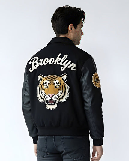Person wearing a black bomber jacket with 'Brooklyn' and a tiger design on the back, against a white background.