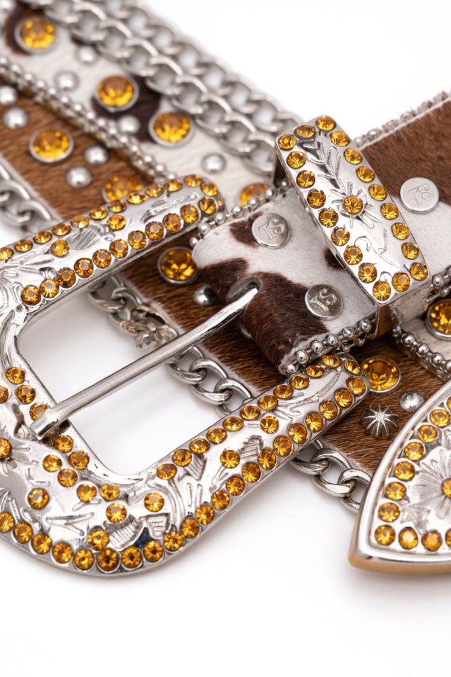 Decorative belt with brown and white cowhide pattern, silver buckle, and orange rhinestones on a white background.