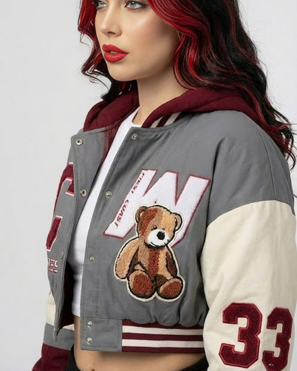 Woman wearing a gray varsity jacket with a teddy bear and number 33 design on a plain background