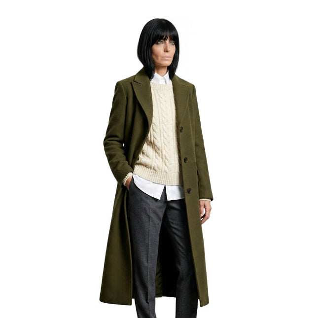 Person wearing a long olive green coat over a cream sweater and dark pants on a white background