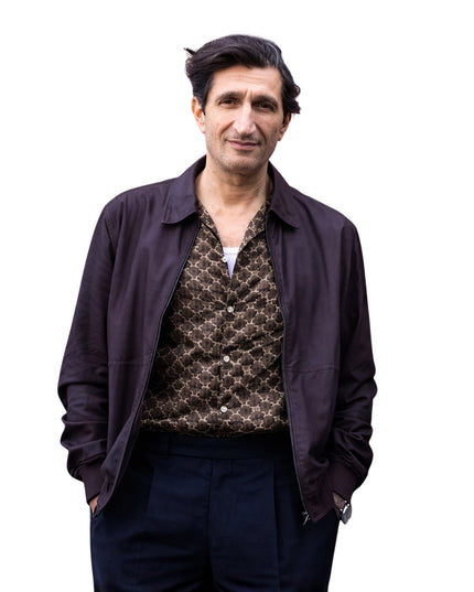 Man wearing a dark jacket over a patterned shirt on a white background