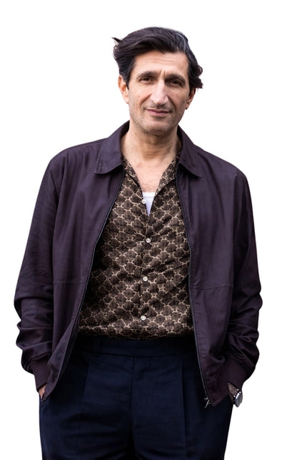 Man wearing a dark jacket over a patterned shirt on a white background