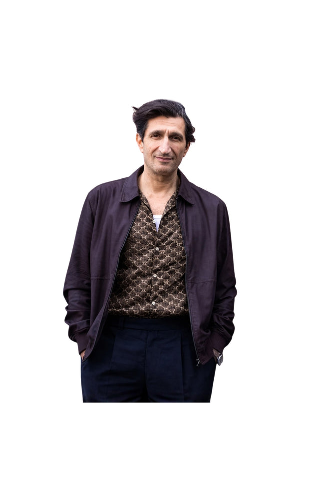 Man wearing a dark jacket over a patterned shirt on a white background