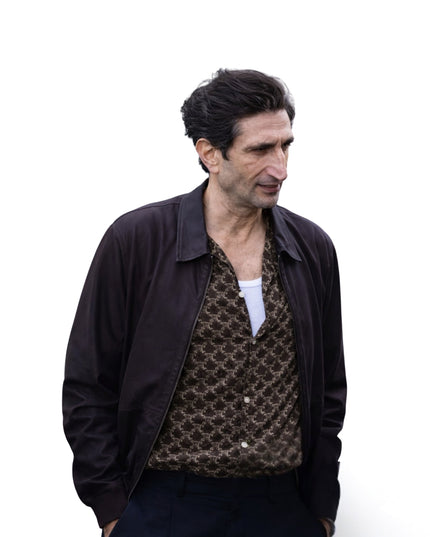 Man wearing a dark jacket over a patterned shirt on a white background