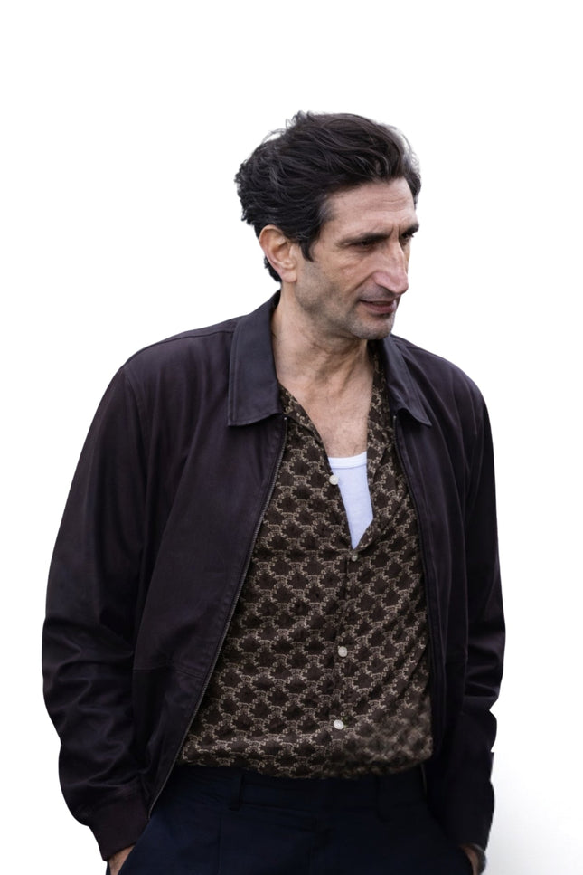 Man wearing a dark jacket over a patterned shirt on a white background