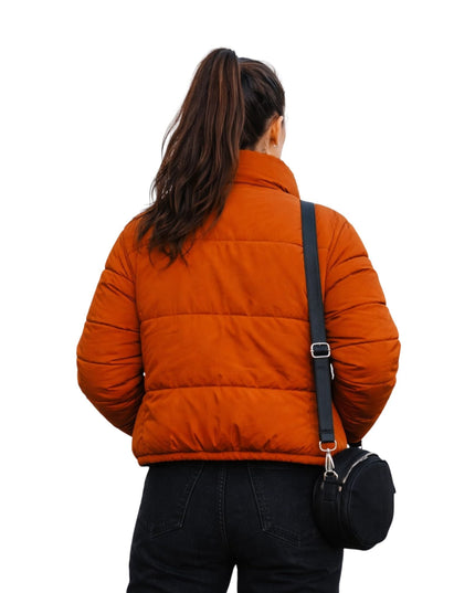 Person wearing an orange puffer jacket with a black bag on a white background