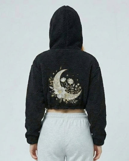 Person wearing a black hoodie with a floral crescent moon design on the back against a light gray background