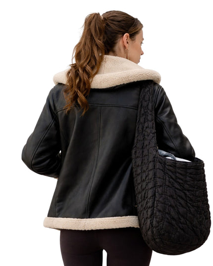 Woman wearing a black leather jacket with beige fur collar holding a textured black bag on a white background