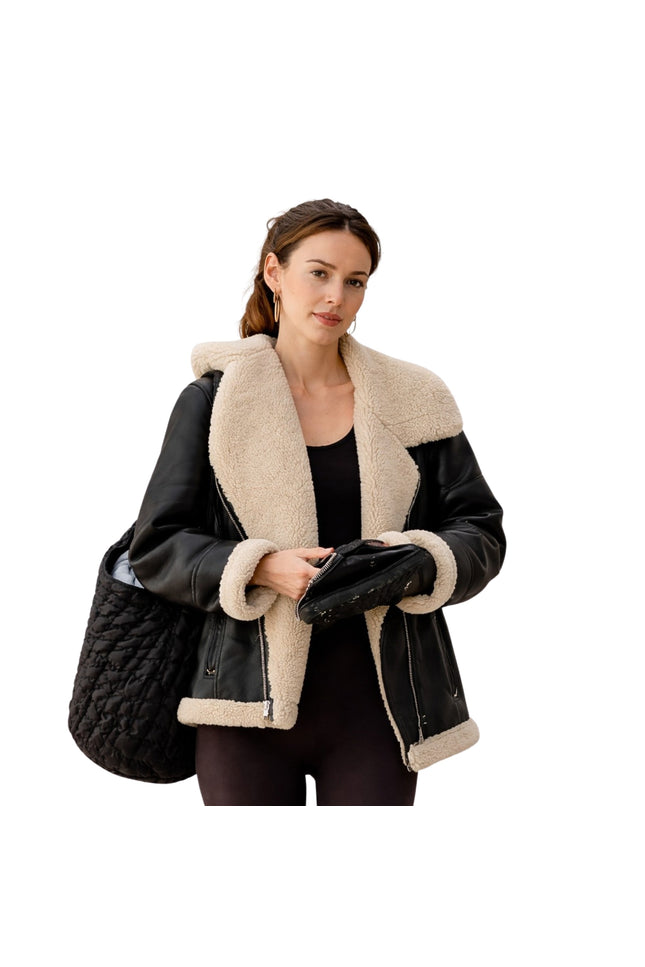 Woman wearing a black leather jacket with beige shearling lining, holding a black quilted bag.