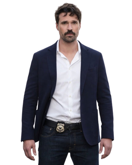 Man wearing a navy blazer, white shirt, and dark jeans on a white background