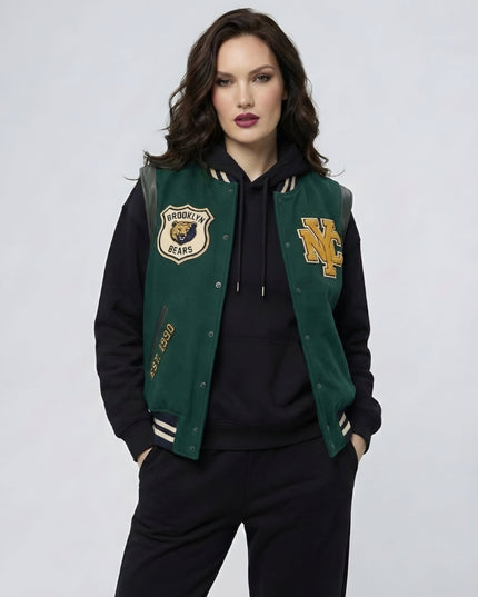 Woman wearing a green and black varsity jacket with logos on a light gray background