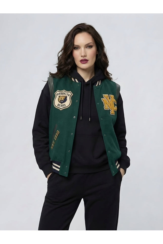 Woman wearing a green and black varsity jacket with logos on a light gray background