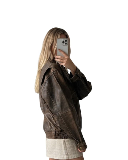 Person wearing a brown jacket taking a mirror selfie on a white background