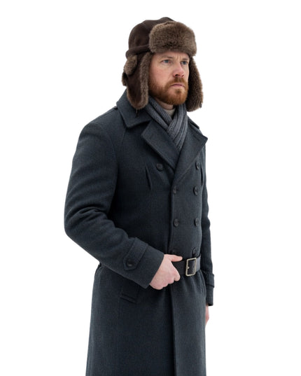 Man wearing a long dark coat and fur hat on a white background