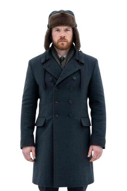 Man wearing a long dark coat and a fur-lined hat on a white background