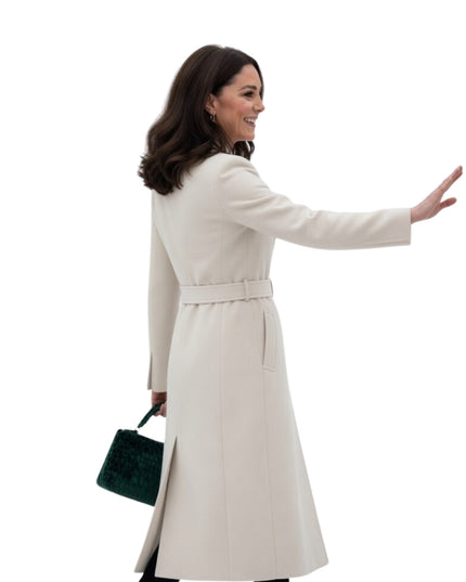 Woman in a beige coat holding a green handbag on a white background
