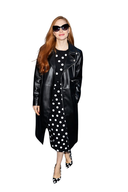 Woman wearing a black leather coat over a black and white polka dot dress on a white background