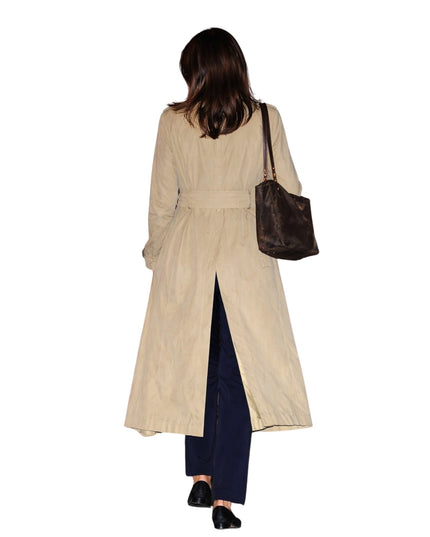 Woman wearing a beige trench coat and holding a brown handbag on a white background