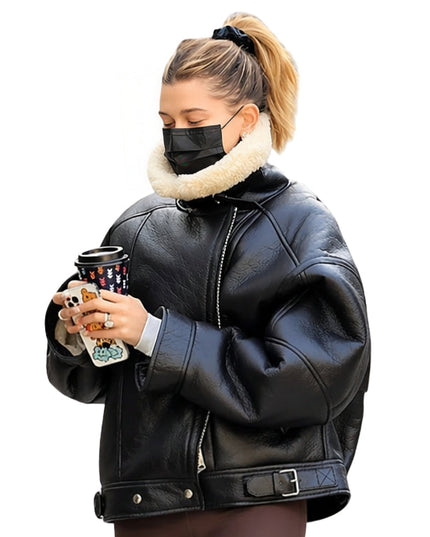 Person wearing a black leather jacket with a white fur collar, holding a Starbucks cup.