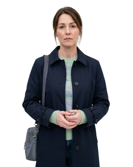 Woman wearing a navy coat and green sweater with a gray bag on a white background