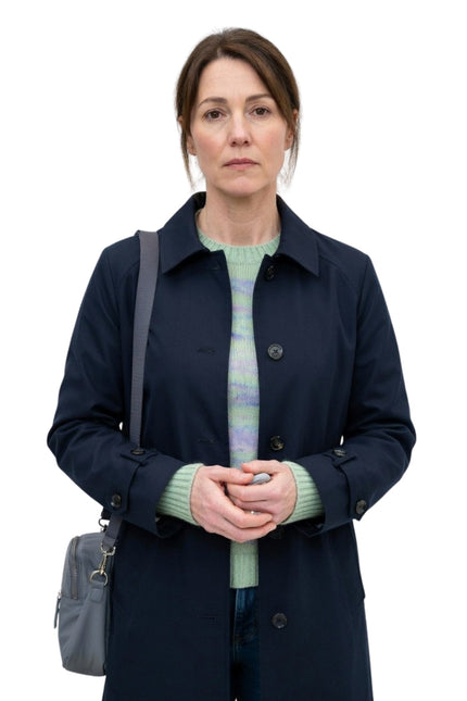 Woman wearing a navy coat and green sweater with a gray bag on a white background