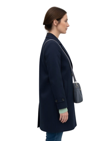Woman wearing a navy coat holding a gray handbag on a white background