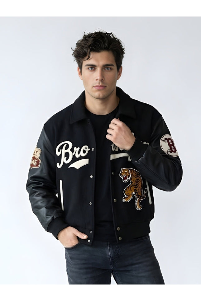 Man wearing a black varsity jacket with patches on a white background