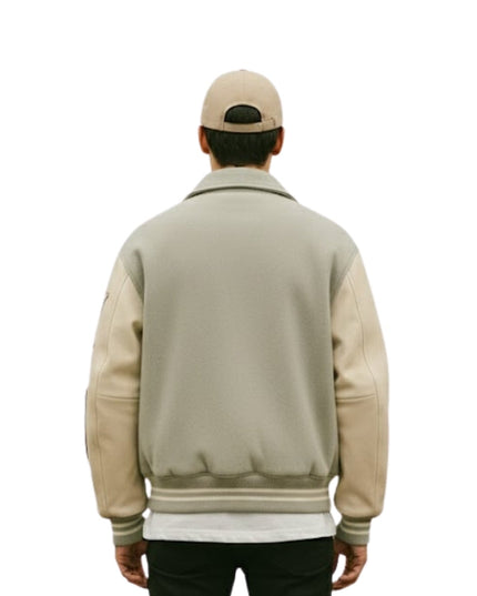 Person wearing a beige varsity jacket with leather sleeves on a white background