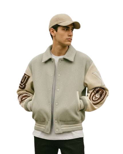 Person wearing a beige varsity jacket with arm patches on a white background