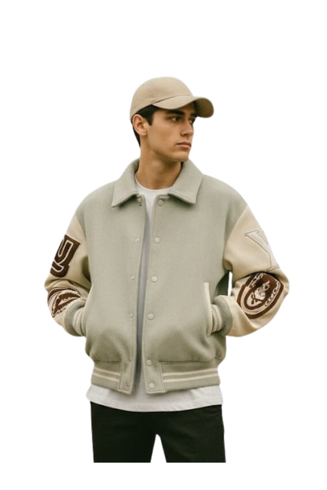 Person wearing a beige varsity jacket with arm patches on a white background