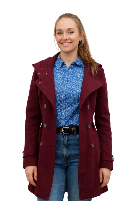 Woman wearing a burgundy coat over a blue shirt and jeans on a white background