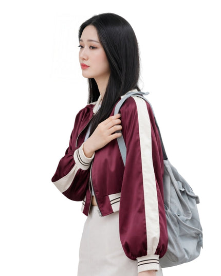 Woman wearing a maroon and white jacket with a gray backpack on a white background