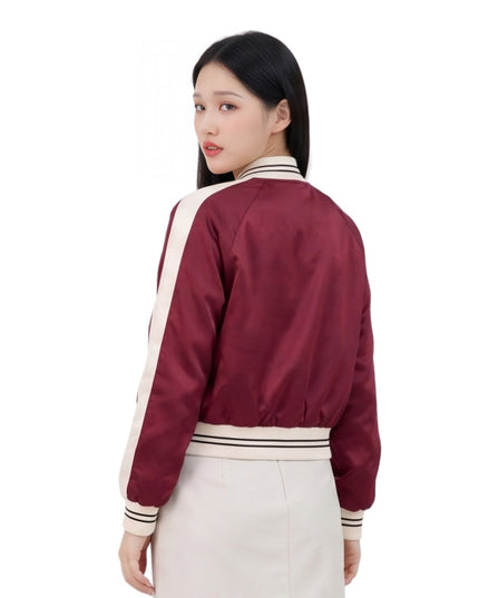 Woman wearing a maroon bomber jacket with white accents on a white background