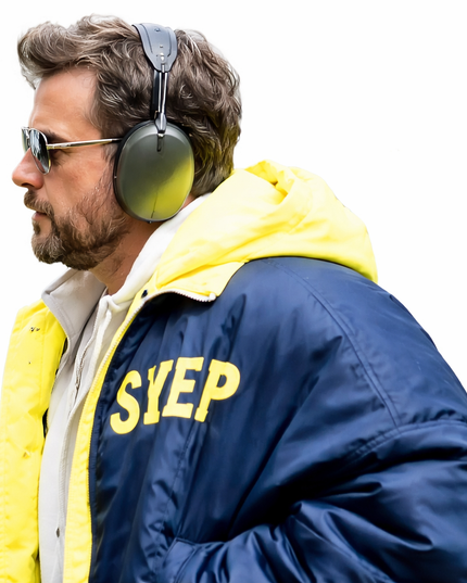 Man wearing a blue jacket with 'SYEP' on it, yellow hood, and headphones on a white background