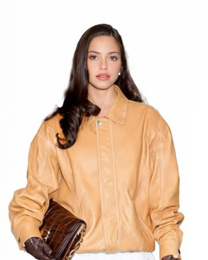 Woman wearing a tan leather jacket holding brown shoes on a white background