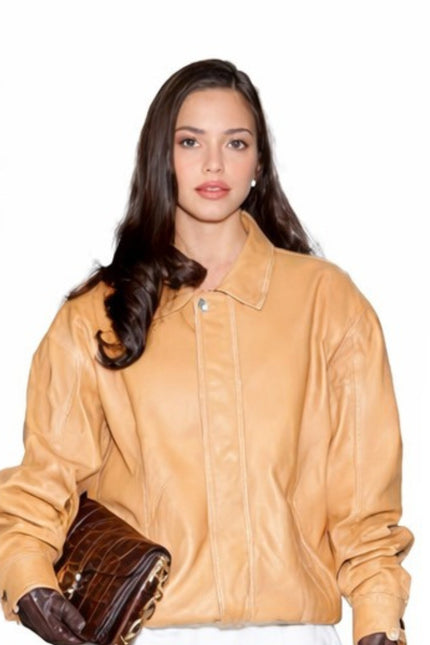 Woman wearing a tan leather jacket holding brown shoes on a white background