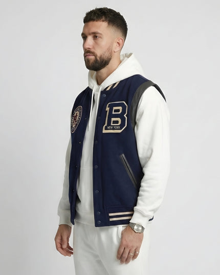 Man wearing a navy varsity jacket with a letter 'B' emblem on a white background