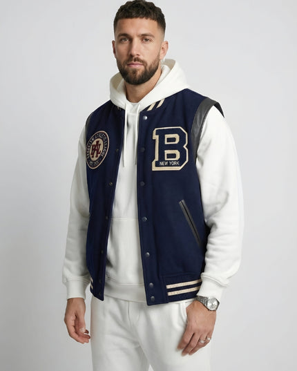 Man wearing a navy varsity jacket with patches on a plain background