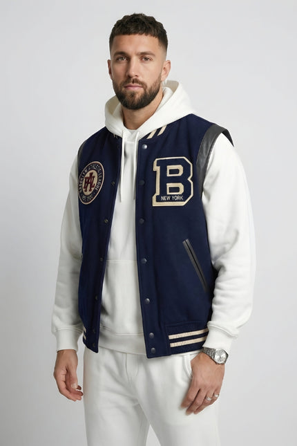 Man wearing a navy varsity jacket with patches on a plain background