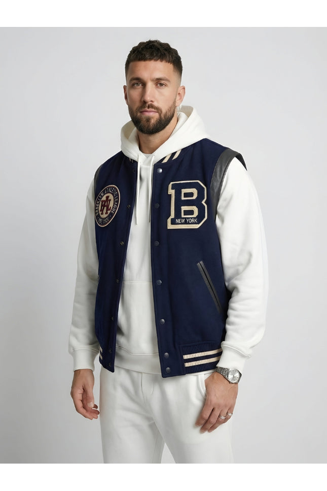 Man wearing a navy varsity jacket with patches on a plain background