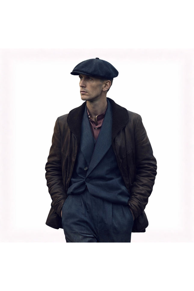 Man wearing a dark coat, gray suit, and flat cap on a white background