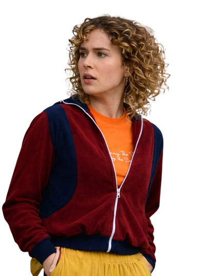 Woman wearing a red and navy tracksuit with an orange shirt underneath on a white background