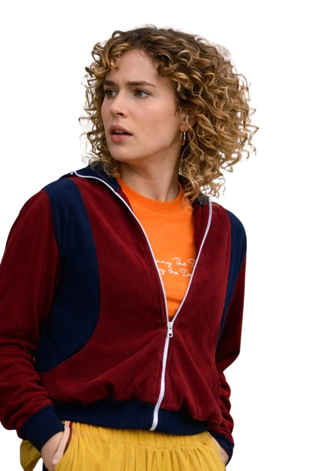 Woman wearing a red and navy tracksuit with an orange shirt underneath on a white background
