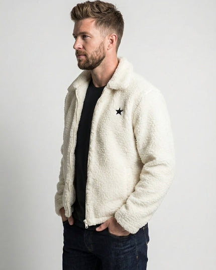Man wearing a white sherpa jacket with a star design on a plain background