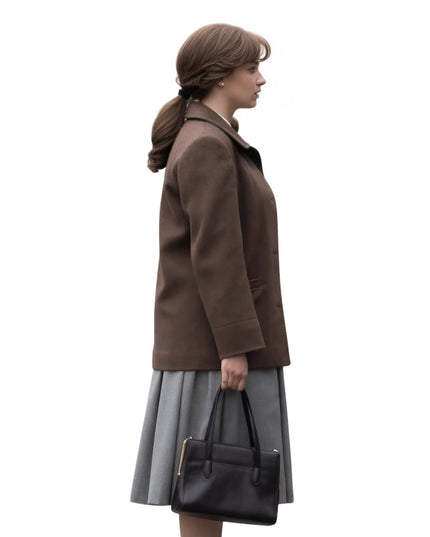 Woman wearing a brown coat and gray skirt holding a black handbag on a white background
