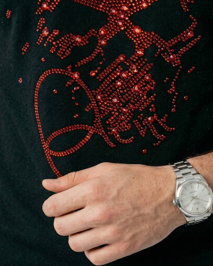 Black garment with red embellishments and a hand wearing a silver watch.